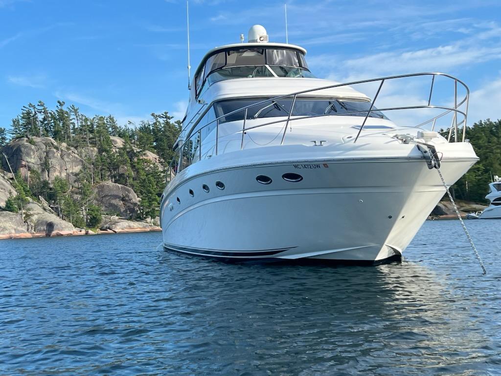 Sea Ray 54 Cockpit Motor Yacht 2001 Sea Ray 54 Cockpit Motor Yacht on serene water with rocky shoreline backdrop.