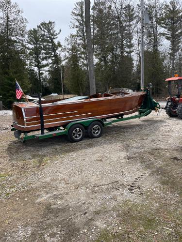 Hacker-Craft 22 Utility 1951 Hacker-Craft 22 Utility boat on trailer, surrounded by trees and gravel path.