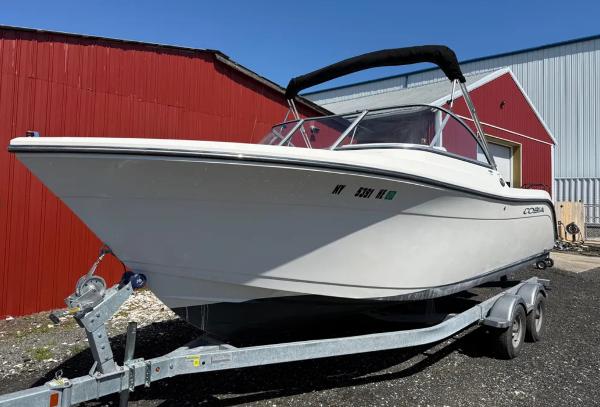 Cobia 220 Dual Console 2021 Cobia 220 Dual Console boat on trailer, parked near red and gray buildings.
