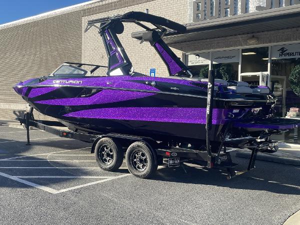 Centurion Fi23 2023 Centurion Fi23 boat with purple and black design on a trailer outside a dealership.