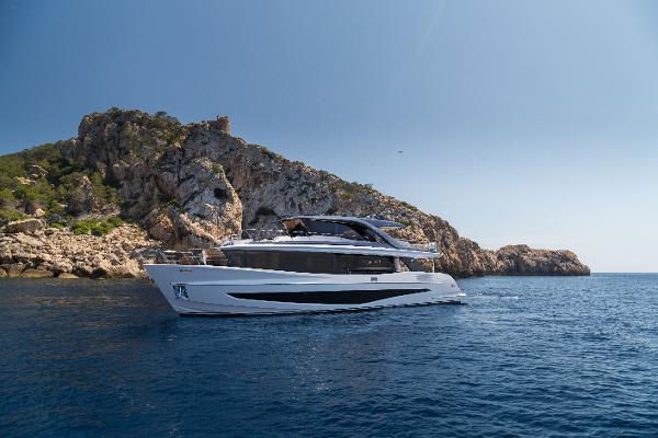 Princess Princess X90 2025 Princess X90 yacht cruising near rocky coastline under clear blue sky.