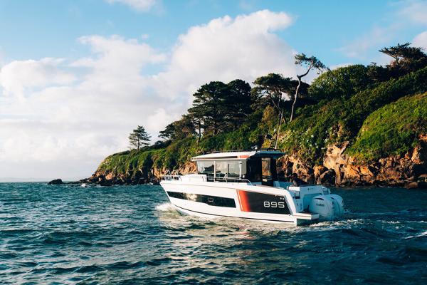 Jeanneau NC895 Sport S2 2026 Jeanneau NC895 Sport S2 cruising near a scenic, tree-lined coastline.