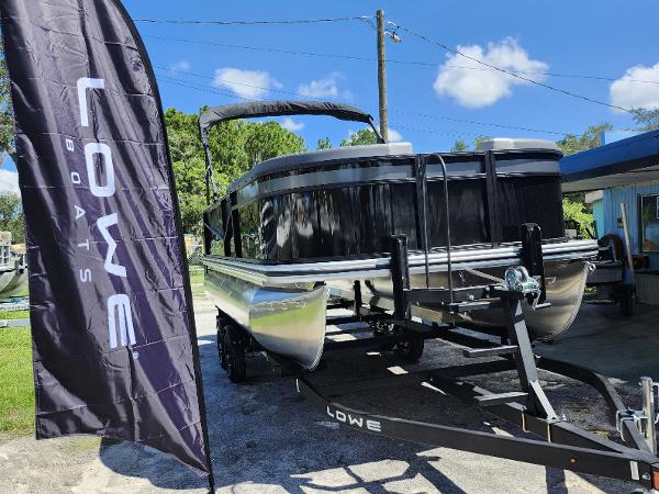 Lowe LS 190 2025 Lowe LS 190 pontoon boat on trailer, displayed outdoors with Lowe Boats flag.