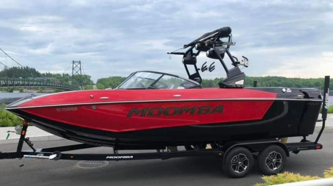 Moomba Mojo 2021 Moomba Mojo boat in red on a trailer, parked near a bridge.