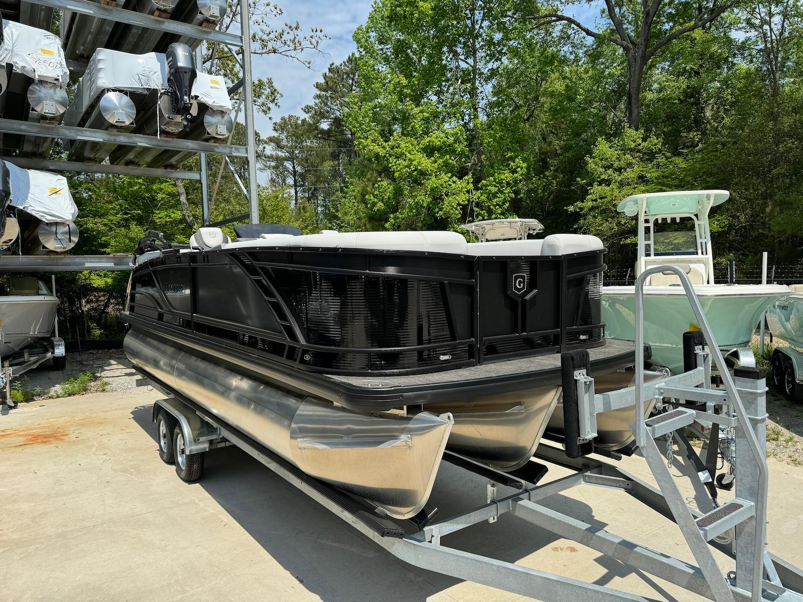 Godfrey Monaco 235 SB 2024 Godfrey Monaco 235 SB pontoon boat on trailer, surrounded by trees and other boats.