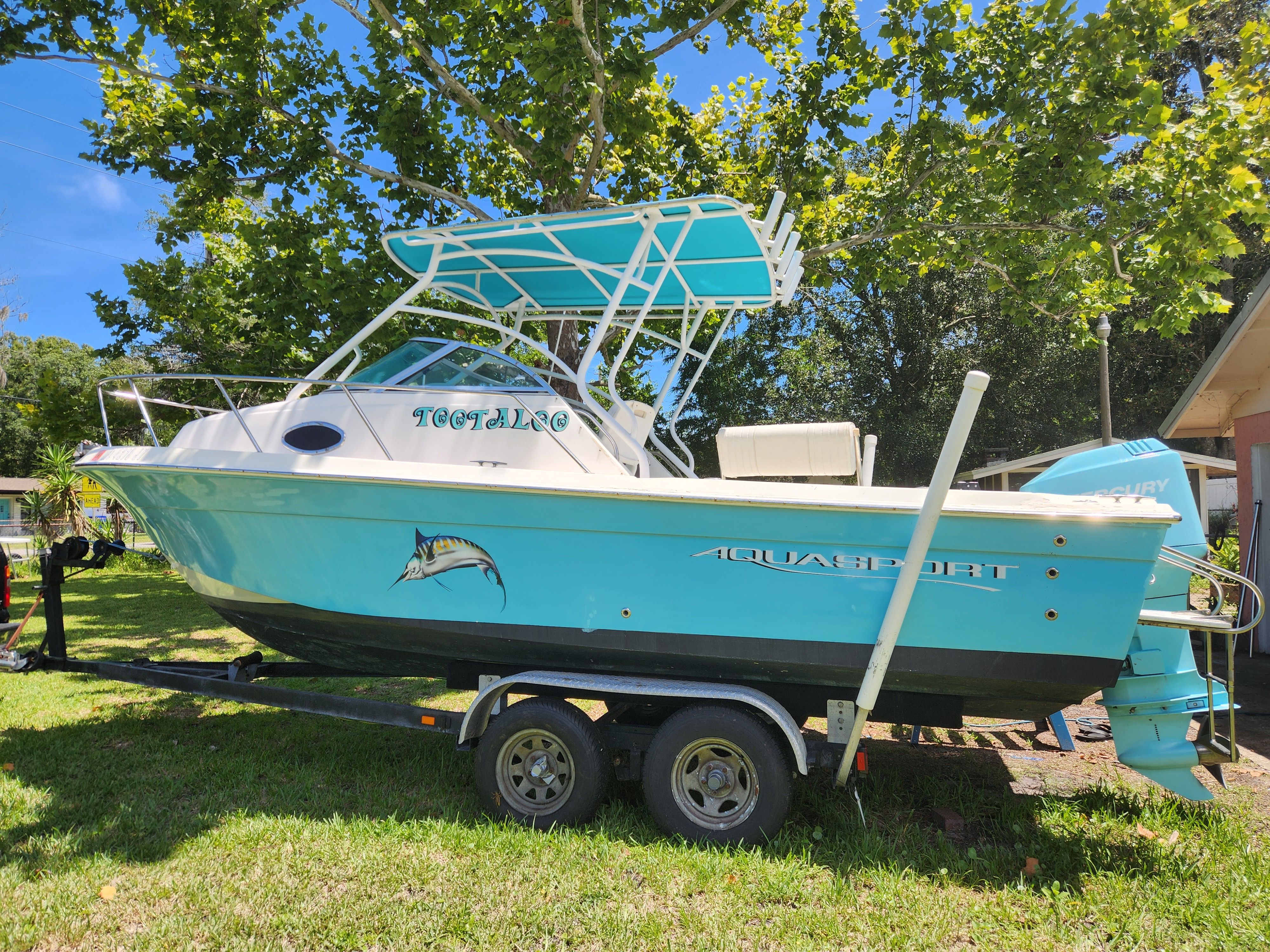 Aquasport Explorer 1997 Aquasport Explorer boat on trailer, turquoise color, parked on grass under trees.