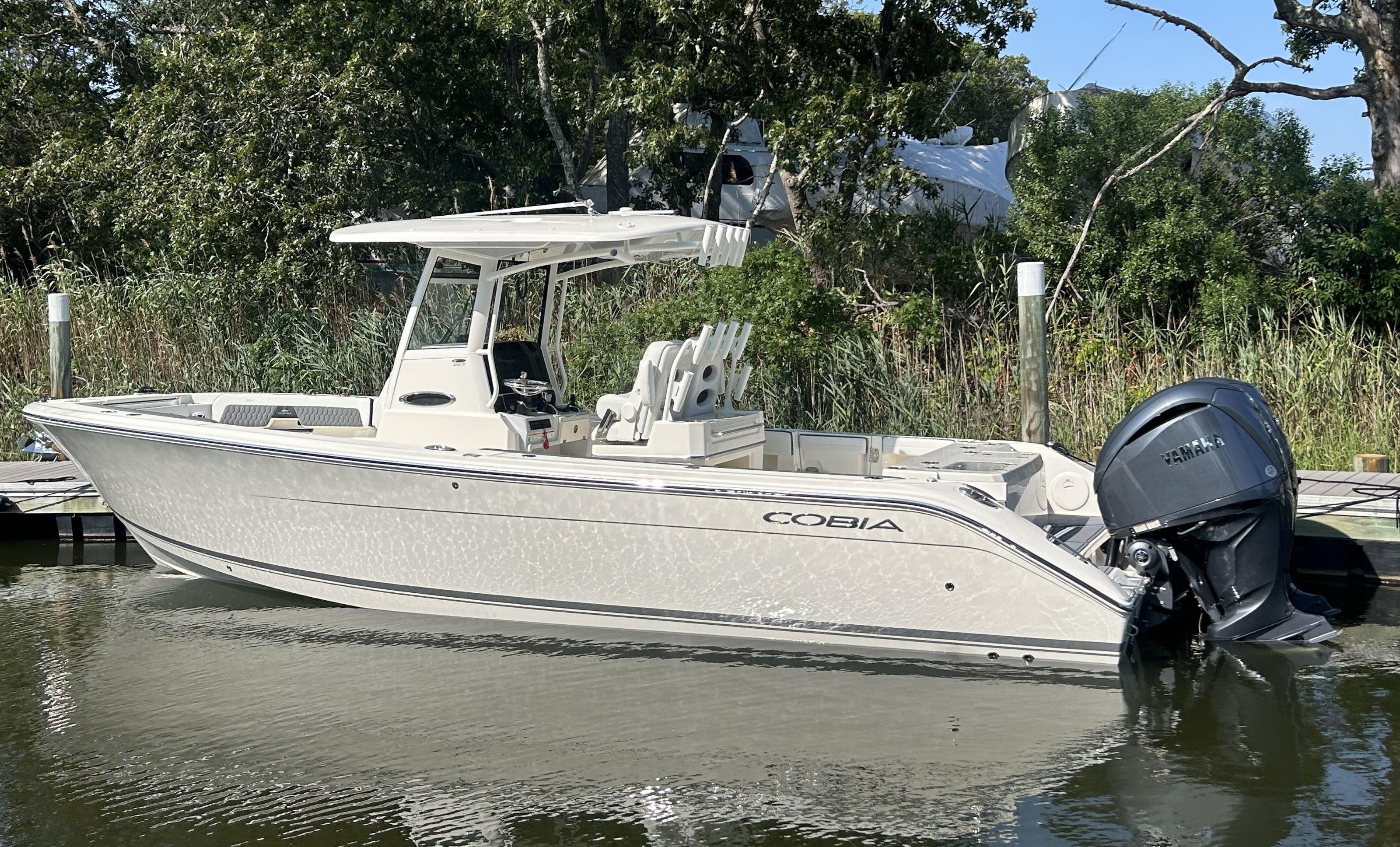 Cobia 285 Center Console 2026 Cobia 285 Center Console boat docked by lush greenery.