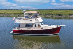 Mainship 34 Trawler 2006 Mainship 34 Trawler on calm water, featuring a red hull and beige canopy.