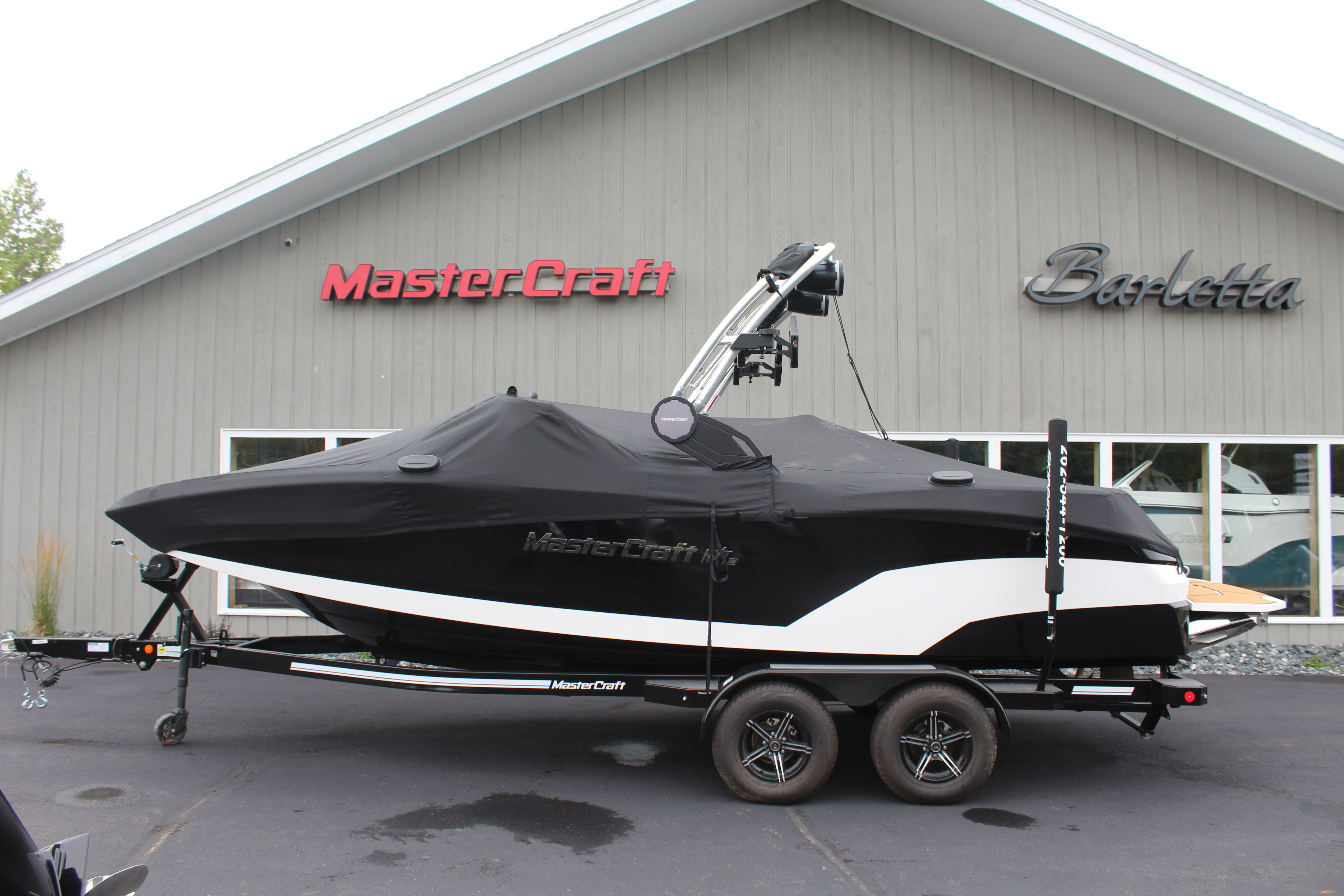 MasterCraft NXT22 2024 MasterCraft NXT22 boat with cover on trailer, parked outside dealership.