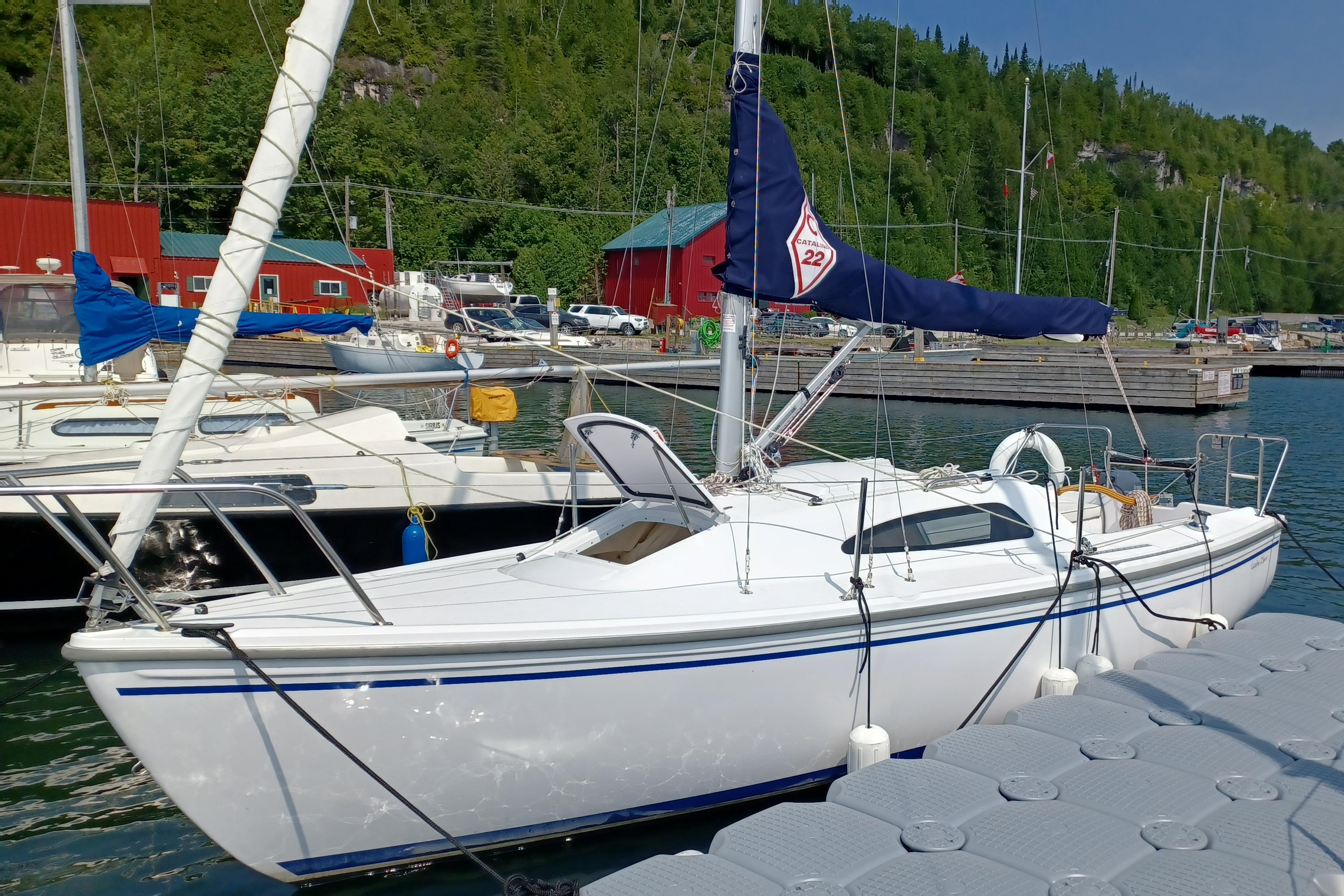 Catalina 22 Sport 2023 Catalina 22 Sport sailboat docked at a marina with red buildings and lush greenery.
