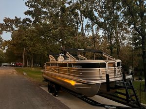 Xcursion X-23RFC 2015 Xcursion X-23RFC pontoon boat on trailer, parked near trees and road.