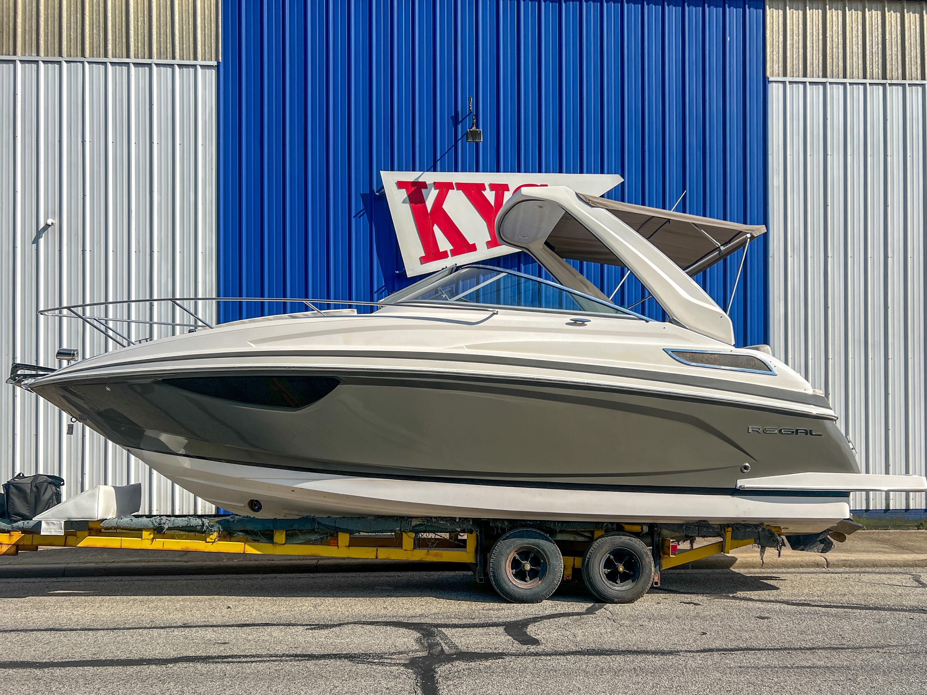 Regal 28 Express 2012 Regal 28 Express boat on trailer, parked by blue and white building.