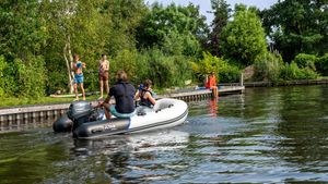 YAM 275Air 2023 YAM 275Air inflatable boat on a scenic lake with people enjoying water activities.