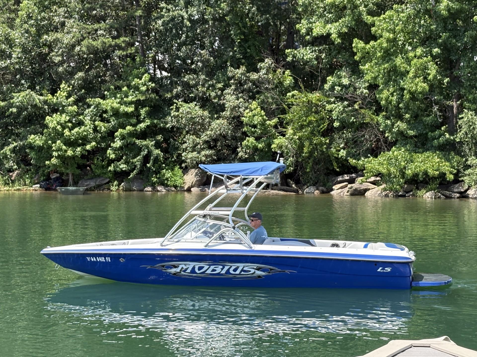 Moomba MOMBIUS LS 2004 Moomba MOBIUS LS boat on a calm lake with lush green trees.