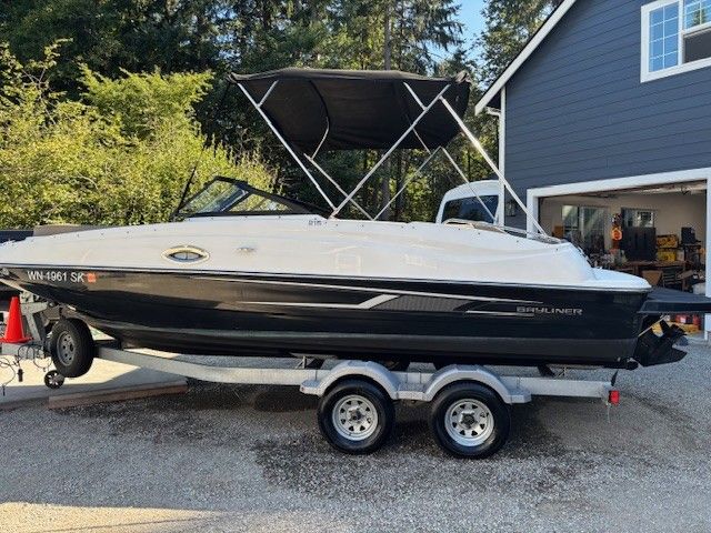 Bayliner 215 Deck Boat 2016 Bayliner 215 Deck Boat on trailer, parked near a house with trees in the background.