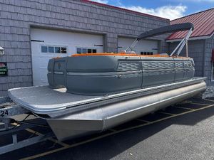 Avalon 2385 Aura Quad Lounge, Twin Toon 2025 Avalon 2385 Aura Quad Lounge pontoon boat, gray with orange accents, parked outside.