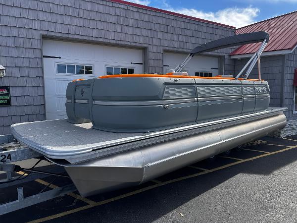 Avalon 2385 Aura Quad Lounge, Twin Toon 2025 Avalon 2385 Aura Quad Lounge pontoon boat, gray with orange accents, parked outside.