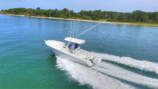 Edgewater 262CC 2023 Edgewater 262CC boat cruising on clear blue water near a forested shoreline.
