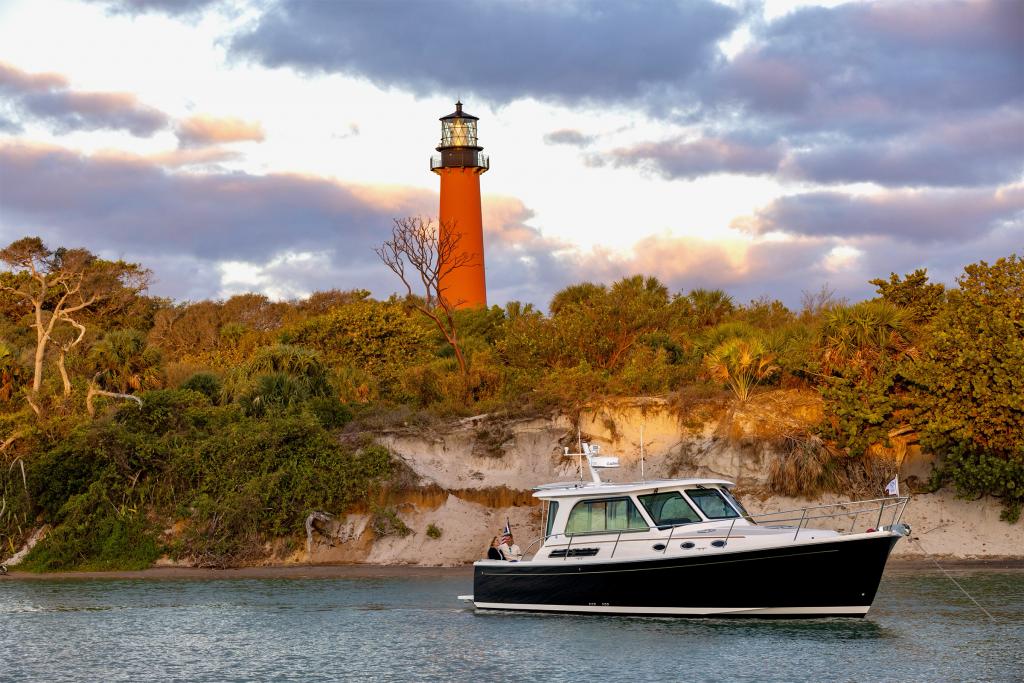 Back Cove 372 2026 Back Cove 372 boat near a scenic lighthouse and lush greenery.