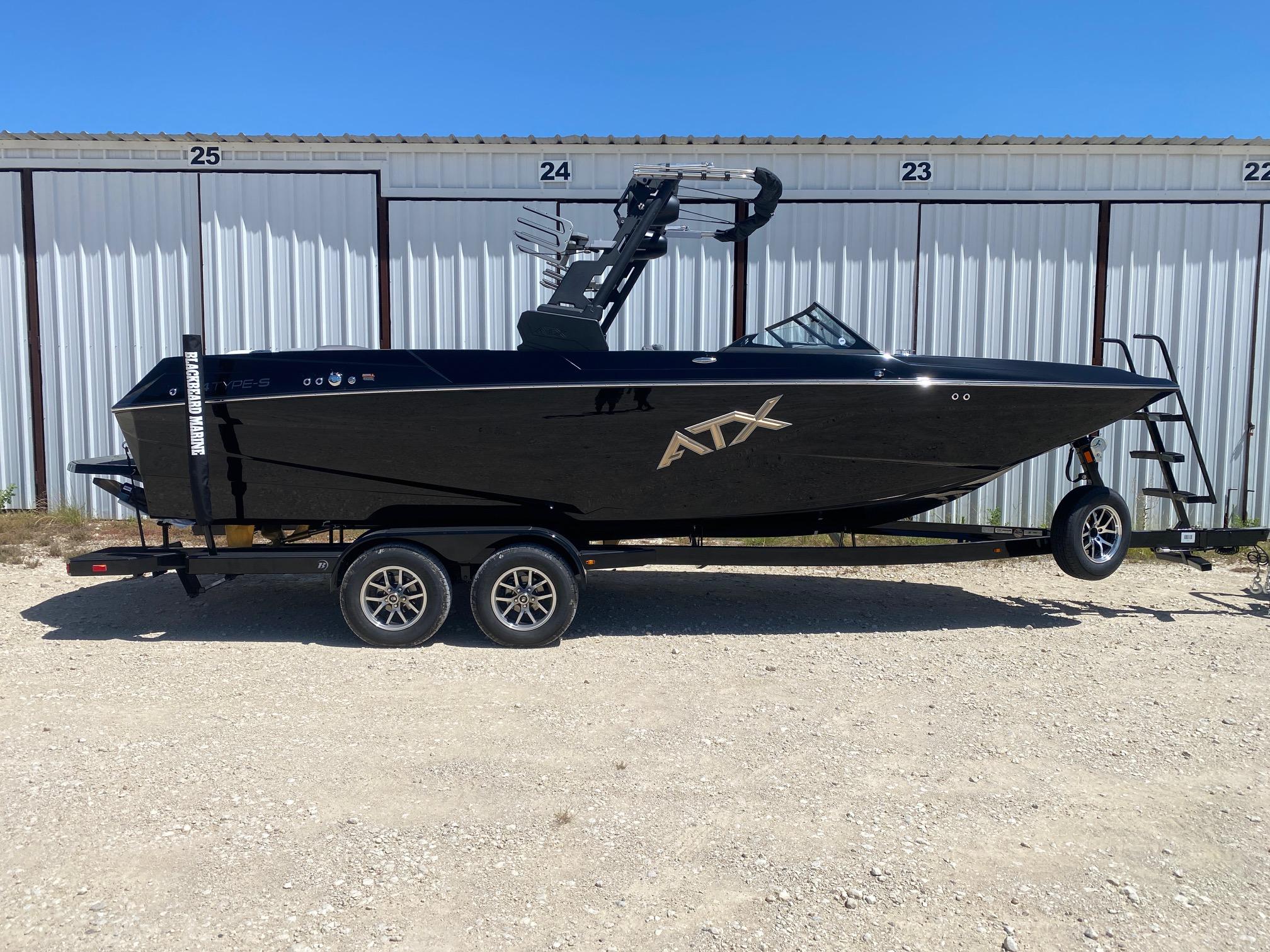 ATX Surf Boats 24 Type-S 2025 ATX Surf Boats 24 Type-S, black, on trailer, parked outside storage units.