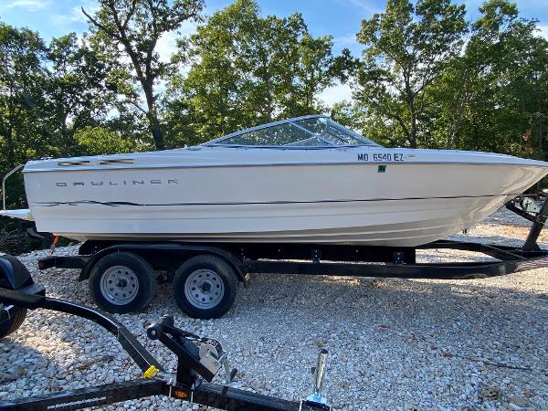 Bayliner 215 Bowrider 2001 Bayliner 215 Bowrider on a trailer, parked on gravel, surrounded by trees.