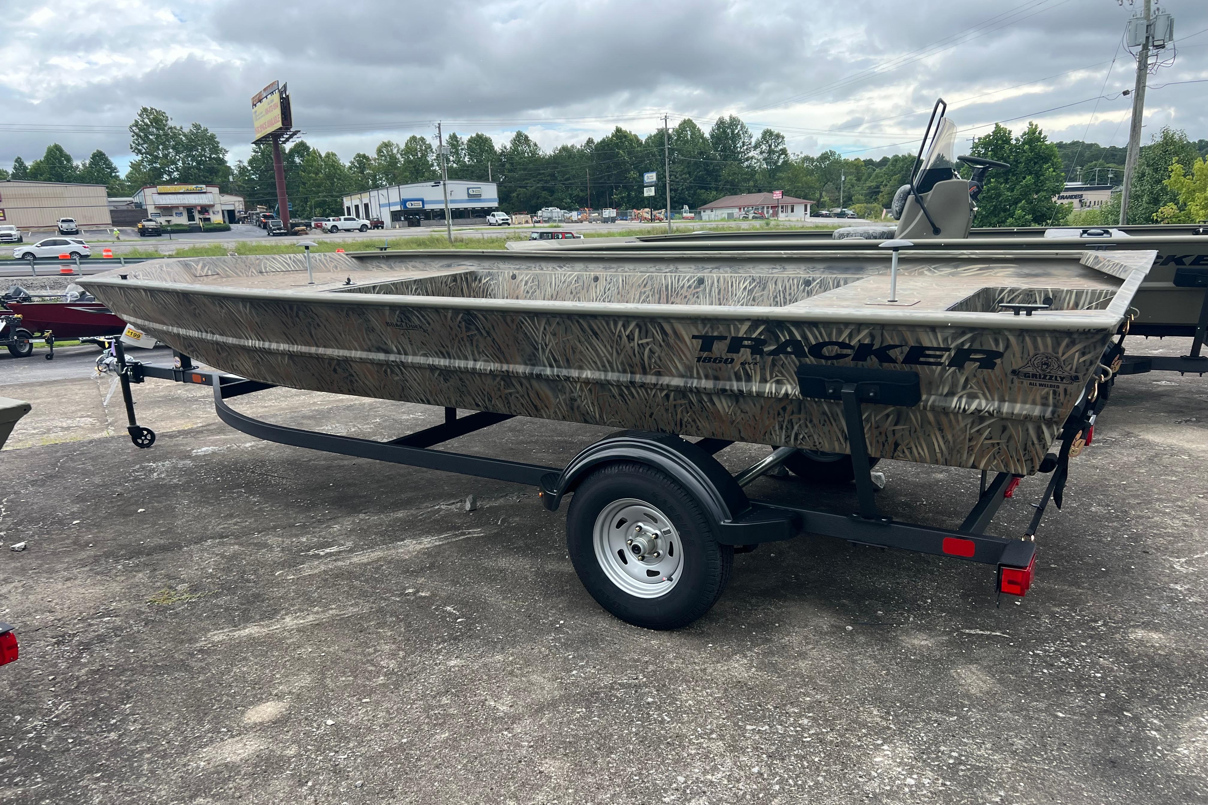 Tracker GRIZZLY 1860 Utility 2026 Tracker GRIZZLY 1860 Utility boat on trailer, camo design, parked outdoors.