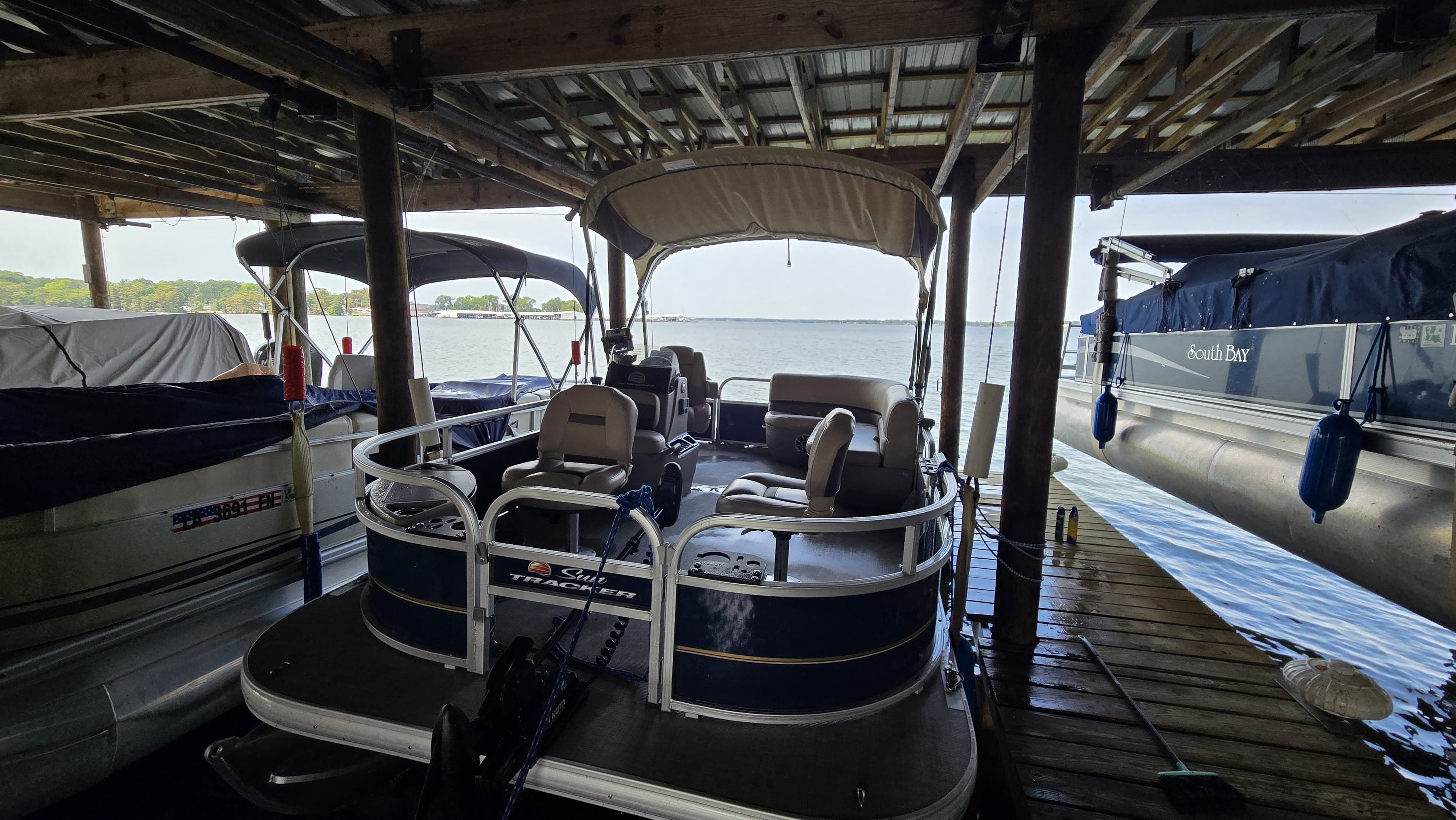 Pontoon Sun Tracker Pontoon 2024 Custom Pontoon boat docked under a wooden shelter by the lake.