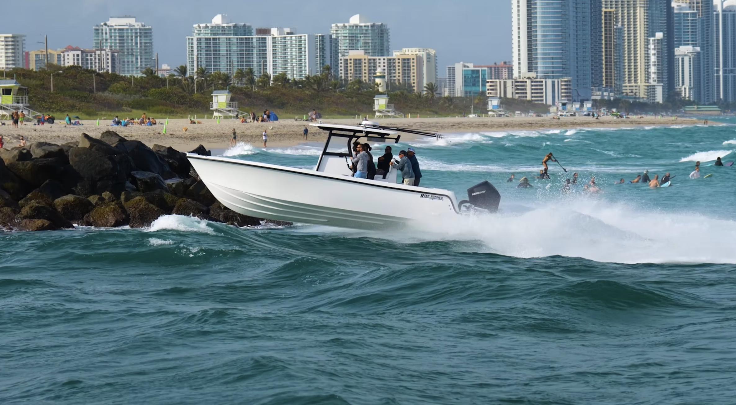 Reef Runner 280 Reef Runner 280 boat navigating waves near a bustling beach, city skyline in background.
