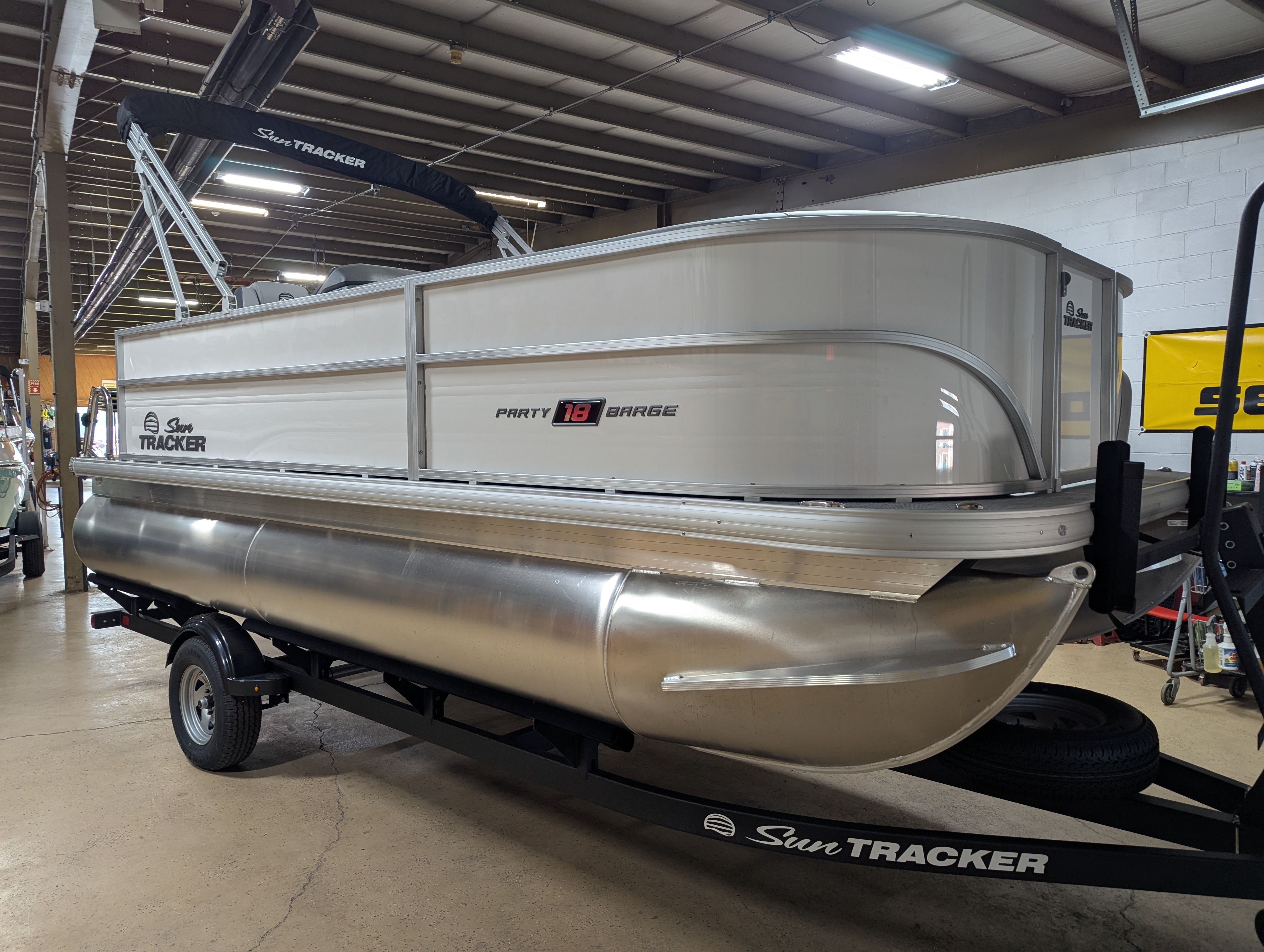 Sun Tracker Party Barge 18 DLX 2026 Sun Tracker Party Barge 18 DLX pontoon boat on trailer in showroom.