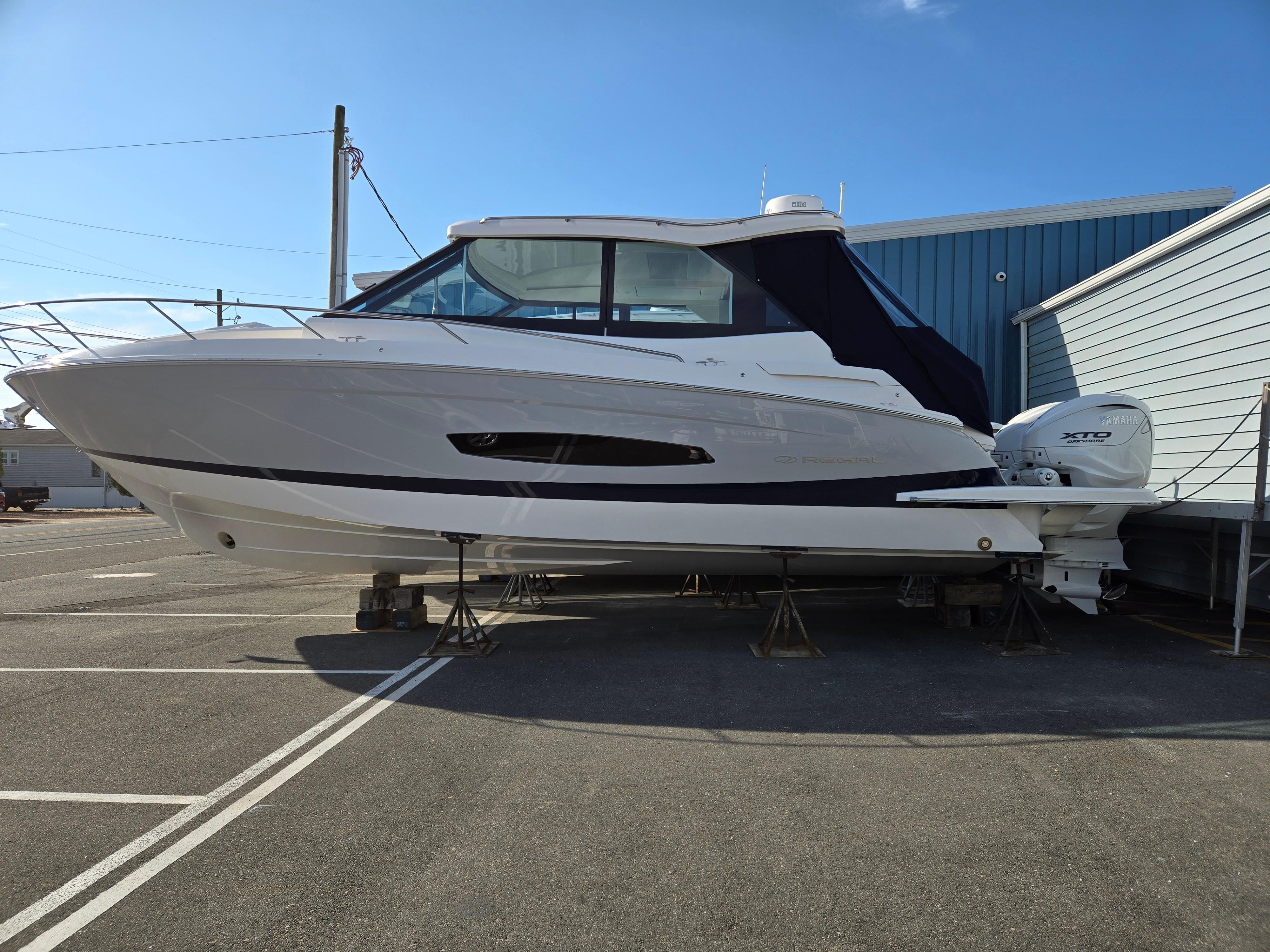 Regal 36 XO 2025 Regal 36 XO boat on stands, side view, in a marina setting.