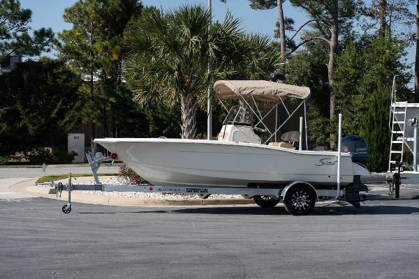 Scout 195 Sportfish 2025 Scout 195 Sportfish boat on trailer, parked outdoors with trees in background.