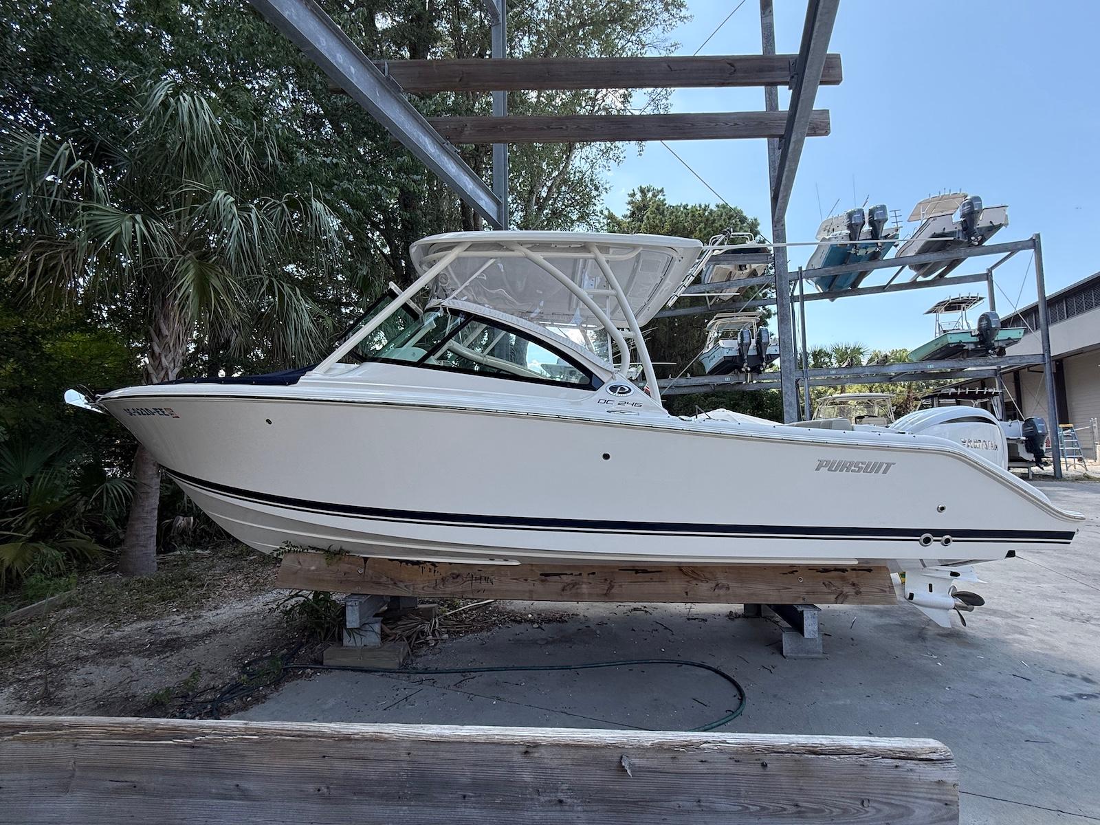 Pursuit DC 246 Dual Console 2023 Pursuit DC 246 Dual Console boat on a wooden stand, surrounded by trees and other boats.