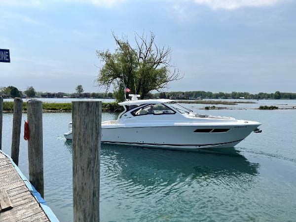 Pursuit DC 365 Dual Console 2024 Pursuit DC 365 Dual Console boat cruising on a serene lake near a dock.