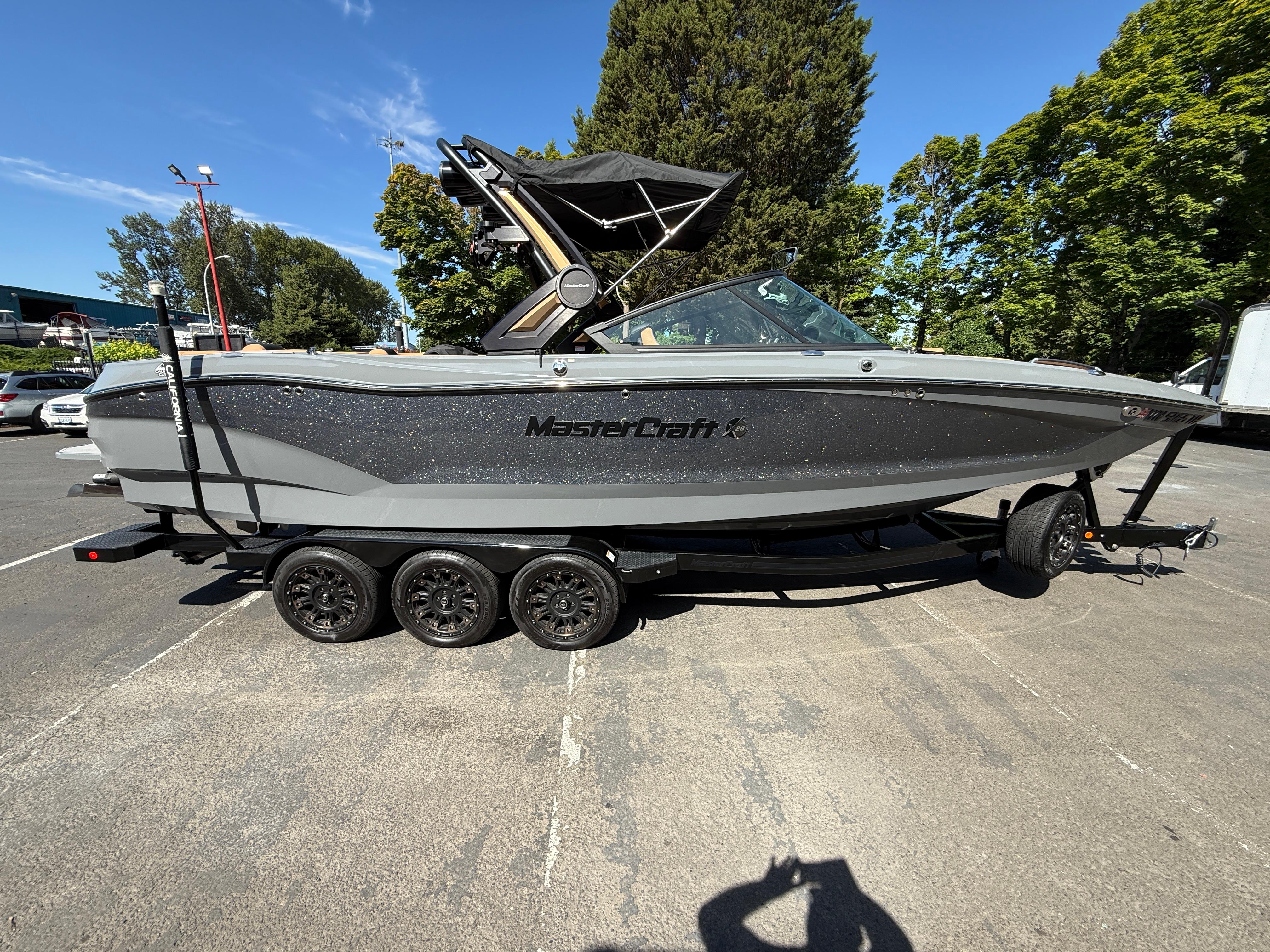 MasterCraft X26 2023 MasterCraft X26 boat on trailer, parked outdoors under clear blue sky.