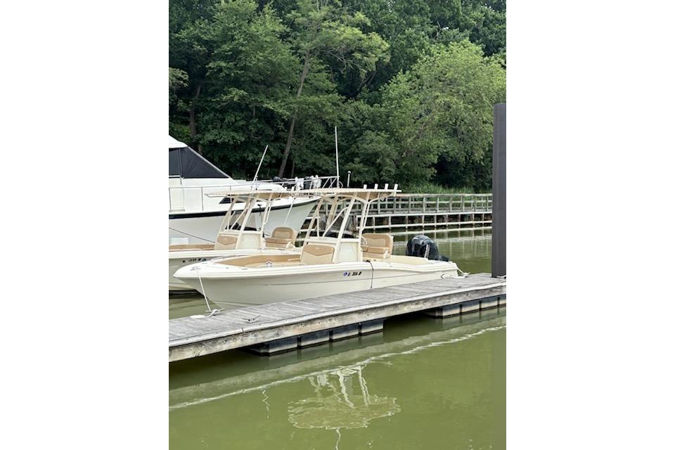 Scout 215 XSF 2023 Scout 215 XSF boat docked on a calm lake with lush greenery.