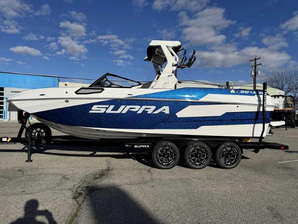 Supra SE 2025 Supra SE boat on trailer, blue and white design, parked outdoors.