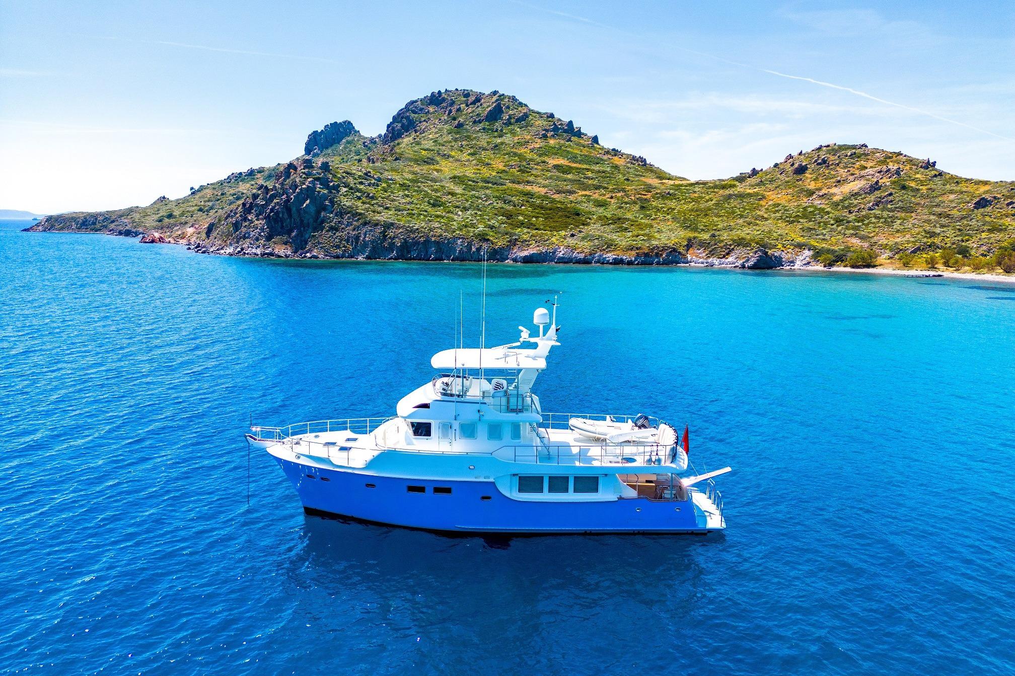 Nordhavn 60 2018 Nordhavn 60 yacht cruising in clear blue waters near a rocky island.
