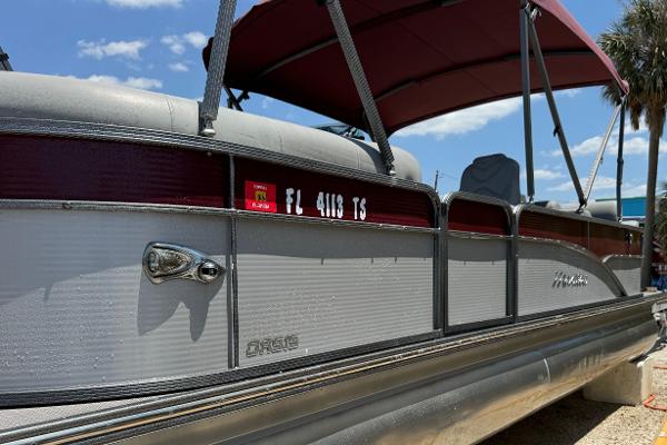 Manitou Oasis SR VP 2022 Manitou Oasis SR VP pontoon boat with maroon canopy, docked under a clear sky.