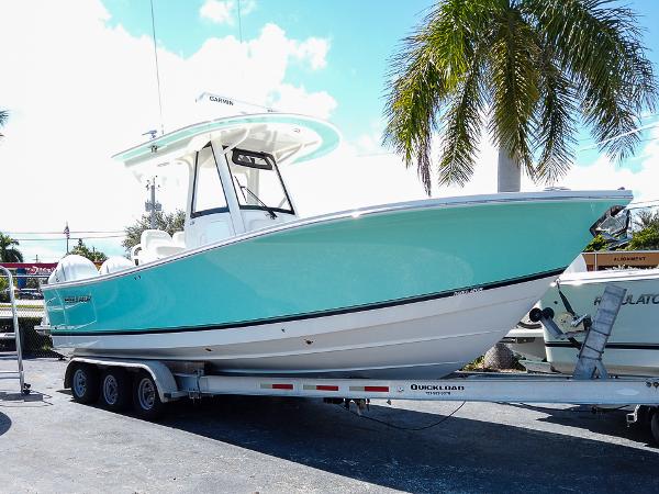 Regulator 28 2024 Regulator 28 boat on trailer, turquoise hull, palm tree background.