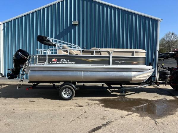 Sun Tracker Party Barge 18 DLX 2023 Sun Tracker PARTY BARGE® 18 DLX pontoon boat on trailer outside blue building.