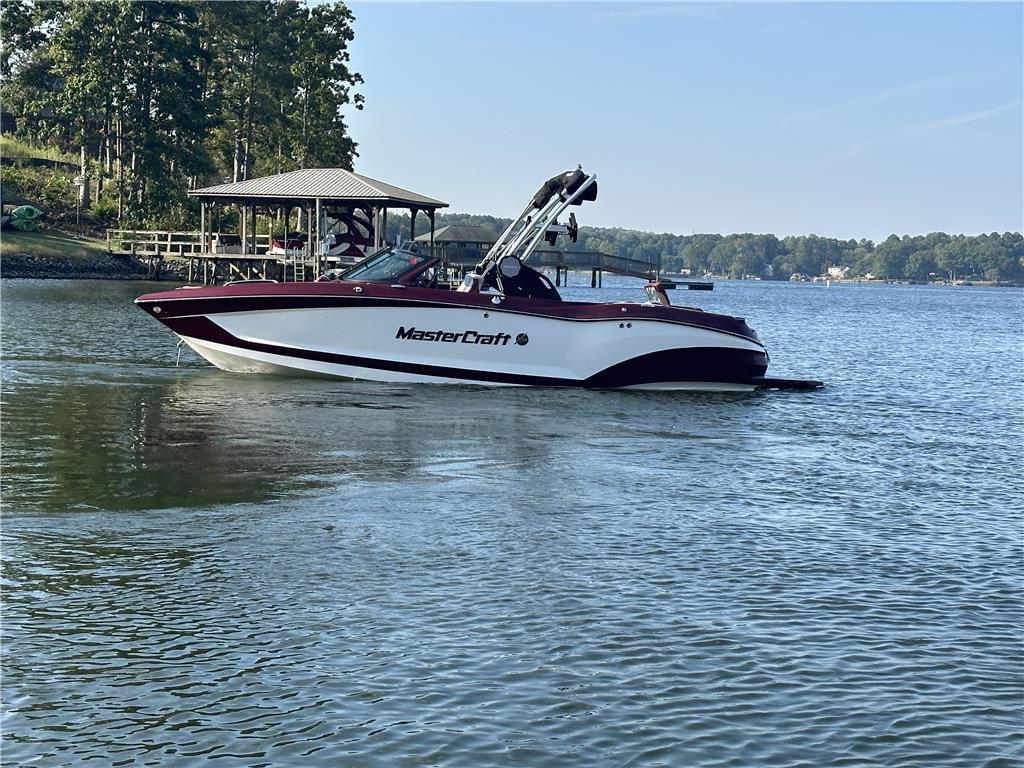 MasterCraft X22 2022 MasterCraft X22 boat on a serene lake with a wooded shoreline.
