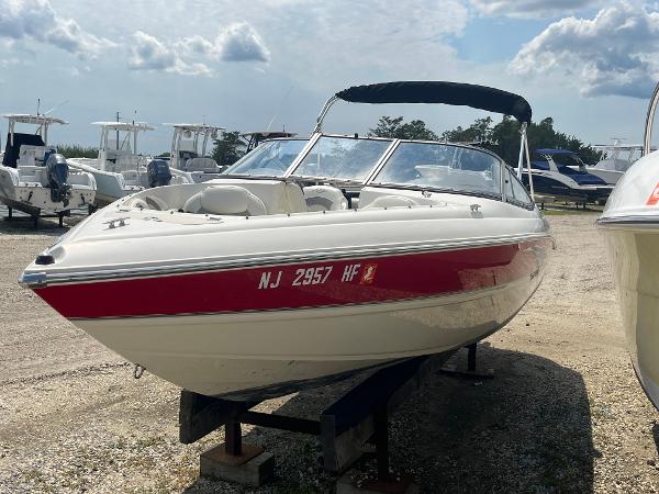 Stingray 225 LR 2013 Stingray 225 LR boat with red stripe, docked on land under a cloudy sky.