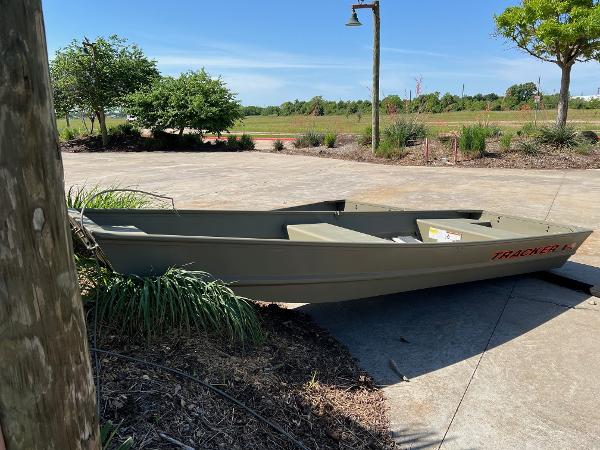 Tracker Grizzly 1436 Utility 2025 Tracker Grizzly 1436 Utility boat on concrete driveway, surrounded by greenery.