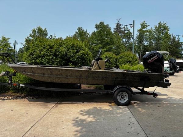 Tracker Grizzly 1860 CC 2025 Tracker Grizzly 1860 CC boat on trailer, parked outdoors, surrounded by greenery.