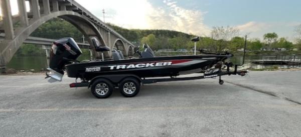 Tracker Savage 215 2025 Tracker Savage 215 boat on trailer, parked near a scenic bridge and river.