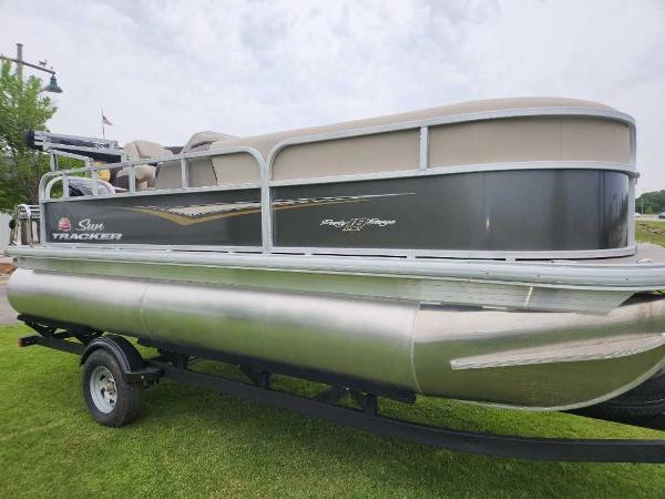 Sun Tracker Party Barge 18 DLX 2025 Sun Tracker Party Barge 18 DLX pontoon boat on trailer, parked on grass.