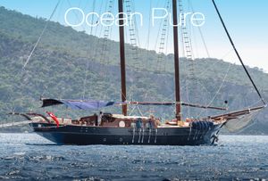 Gulet 99.7 Sailing Yacht Ocean Pure, 1993, cruising on serene waters with lush green hills in the background.