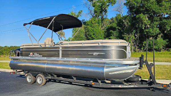 Sun Tracker Party Barge 24 DLX 2024 Sun Tracker Party Barge 24 DLX pontoon boat on a trailer, parked outdoors.