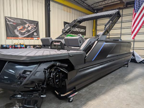 Manitou Explore Dual Engine 2025 Manitou Explore Dual Engine boat in a showroom with American flag.