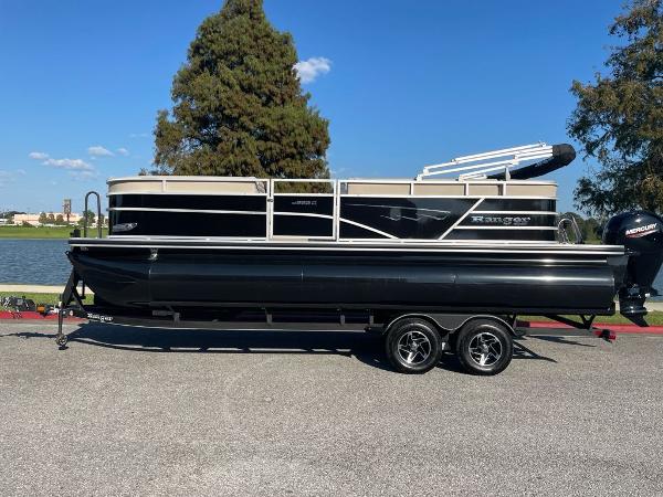 Ranger Reata 223C 2024 Ranger Reata 223C pontoon boat on trailer by a lake.